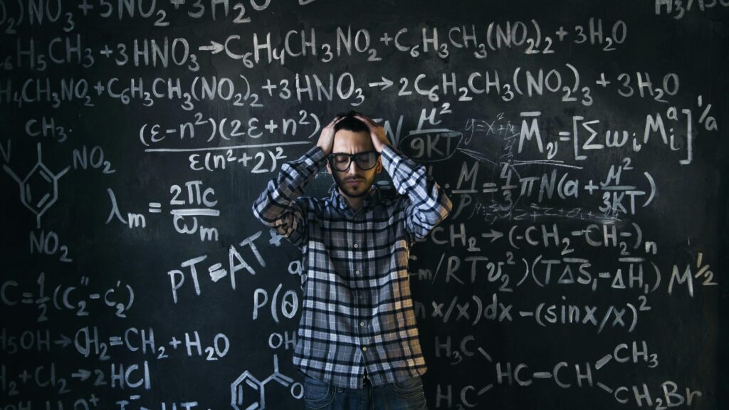 Man in glasses focusing on math problems, struggling with complex equations on chalkboard.